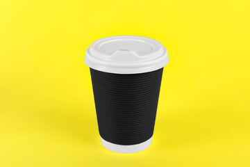 Black paper cup with plastic lid on yellow background. Coffee to go