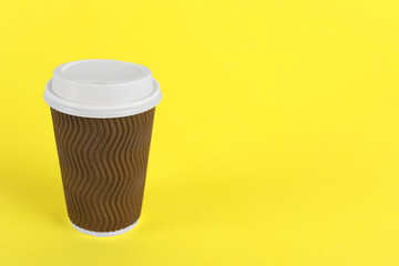 Brown paper cup with plastic lid on yellow background, space for text. Coffee to go