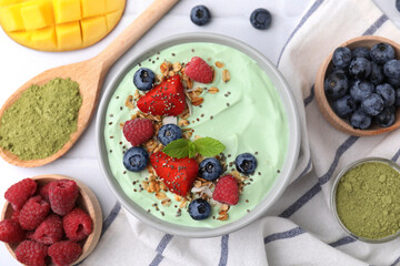 Tasty matcha smoothie bowl served with berries and oatmeal on white tiled table, flat lay. Healthy breakfast