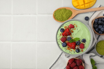 Tasty matcha smoothie bowl served with berries and oatmeal on white tiled table, flat lay with...