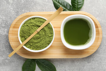 Green matcha powder, bamboo scoop, fresh beverage and leaves on light grey table, flat lay
