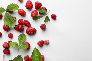 Many fresh wild strawberries and leaves on white background, flat lay. Space for text
