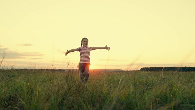 Positive little girl runs spreading arms for embrace in country field at sunset