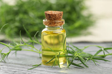 Bottle of essential oil and fresh tarragon leaves on grey wooden table