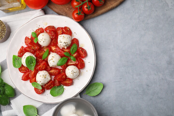 Tasty salad Caprese with tomatoes, mozzarella balls, basil and ingredients on grey background, flat lay. Space for text