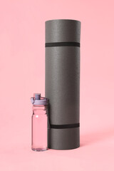 Grey yoga mat and bottle of water on pink background