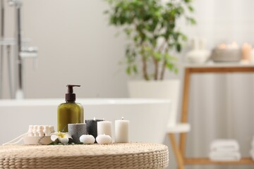 Obraz na płótnie Canvas Spa products, burning candles and plumeria flower on wicker table in bathroom. Space for text