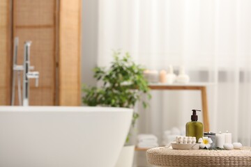 Fototapeta na wymiar Spa products, burning candles and plumeria flower on wicker table in bathroom. Space for text