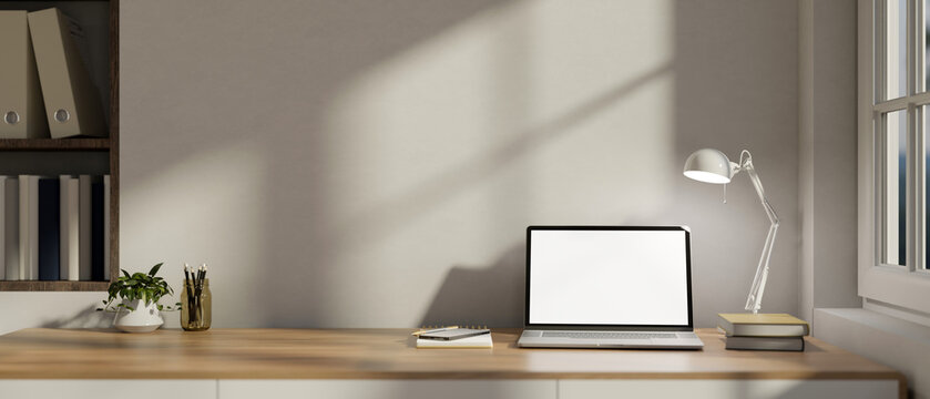 Fototapeta A laptop on a wooden desk against the white wall in a modern minimalist home office.