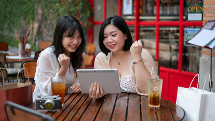 Two excited and surprised Asian female friends are watching an interesting video on a tablet.