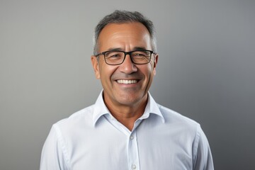Generative AI : Portrait of a mature businessman wearing glasses on grey background. Happy senior latin man looking at camera isolated over grey wall with copy space. Close up face of happy successful - obrazy, fototapety, plakaty