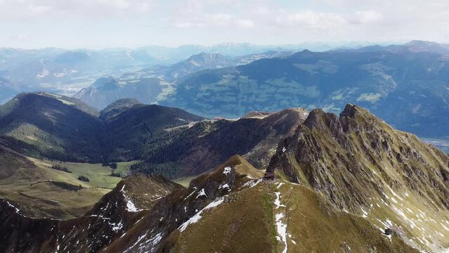 Cinematic aerial of alps mountain top with old wooden chapel on steep peak. Beautiful alpine scenery with valley in distance landscape view. Kellerjoch, Austria. Drone flying around summit, sunny day