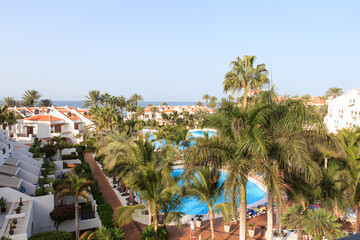 Fototapeta na wymiar Hotel resort panorama with swimming pool, palm trees and view of the Atlantic Ocean in Playa de las Americas, Tenerife