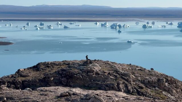 Lonely travaler looks at floating icebergs in the distance. Immikkeertikajik, Scoresbysund, Greenland.