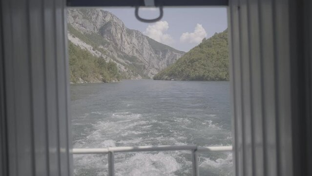 A Ferry trip in Albania from Fierze to Koman over the lake with a majestic nature around on a sunny day with clouds looking over the river seen from the back of the boat in between two walls LOG