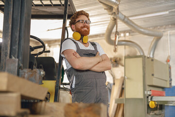 Fototapeta na wymiar Portrait of smiling carpenter in eyeglasses standing on the background on carpentry workshop