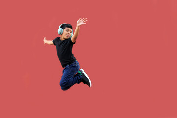9-year-old dark-skinned Latino boy jumps with happiness while listening to music in his headphones