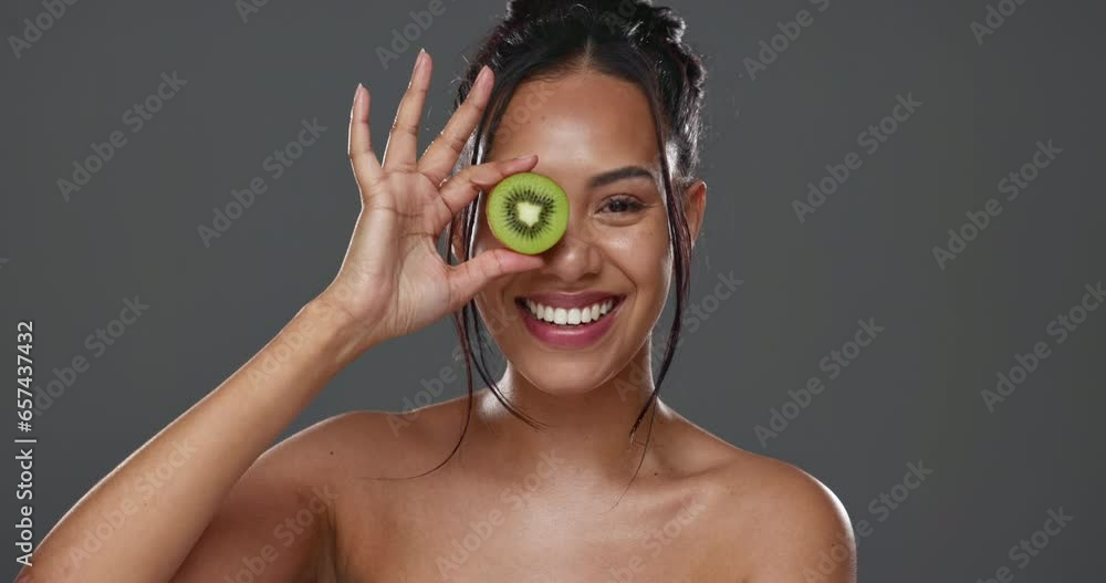 Wall mural Woman, kiwi and beauty in studio for health, diet and smile on face for skincare by background. Girl, model or happy for nutrition choice, vegan food and fruit on eye for wellness with natural glow