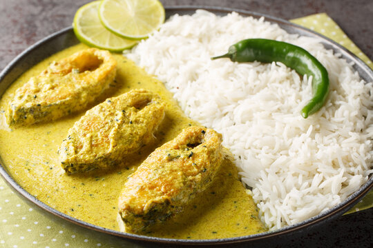 Portion of the popular Hilsa or Ilish fish stewed in mustard sauce with a side dish of white rice close-up in a plate on the table. horizontal