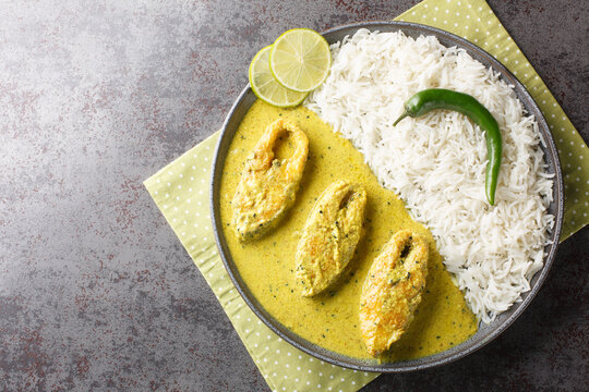 Bengali Shorshe Ilish or Hilsa cooked in Mustard Gravy served with white rice closeup on the plate on the table. Horizontal top view from above