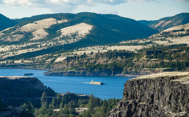 A barge filled with wheat for animal feed being pushed by a tugboat upstream in the Columbia River Gorge. Seen from Tom McCall Preserve in Mosier, Oregon - obrazy, fototapety, plakaty