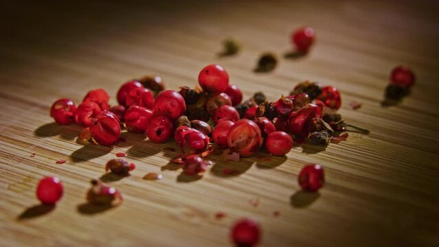A pile of pink peppercorn on a wooden surface with dramatic lighting, camera orbiting