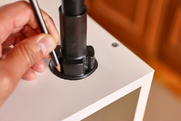 Holes for fastening the furniture leg are marked with a pencil. Assembling cabinet furniture.