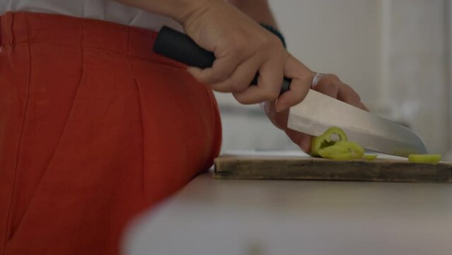 Static, close up of a woman cutting a green pepper with a chef knife. 4K with Panasonic Lumix S5 and a 75mm lens.