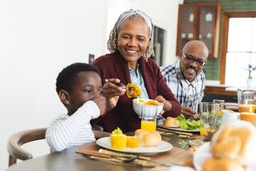 Happy african american grandmother serving food for grandson at thanksgiving dinner