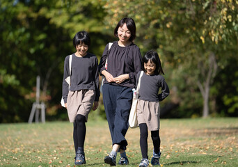トートバッグを肩にかけて公園を一緒に歩く母娘3人（2）