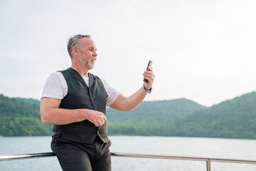 Happy senior using smart phone while walking on Yacht having fun in a sunny day, activity after retirement in vacations and summer.