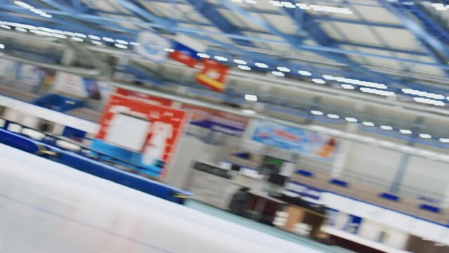 Dutch tilt slowmo shot of two Caucasian male athletes in speed skating uniforms sprinting and competing during practice in indoor ice rink