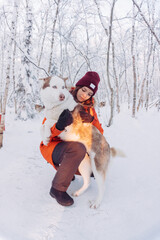 girl in a bright orange jacket sits and plays and hugs with a husky breed dog in the winter forest after snowfall during frost in the rays of the bright sunset sun