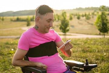A young gay man in a wheelchair using a mobile phone in the park at sunset.