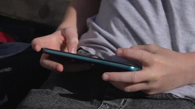 Close-up of a blue smartphone in the hands of a teenager on the street.