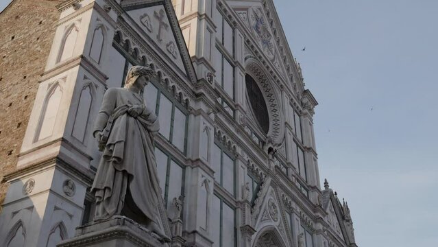 Statue of Dante Alighieri with a Laurel wreath on his head and an eagle at his side in Florence with the Basilica of Santa Croce in the background.