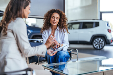 Happy woman buying a car and closing the deal with a handshake with the saleswoman at the...