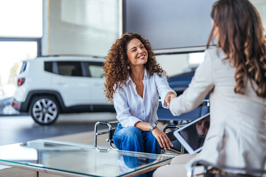 Happy woman buying a car and closing the deal with a handshake with the saleswoman at the dealership. Smiling car saleswoman discussing a contract with a female customer.