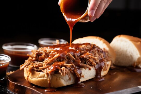hand smearing sauce on pulled pork for a barbecue sandwich