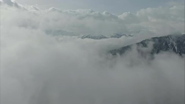 An idyllic aerial vista unfolds, showcasing a mountain range veiled beneath a low layer of clouds, with snow-capped peaks piercing through the mist.