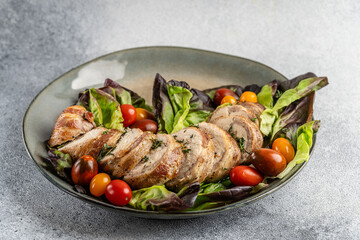 Turkey roll with chicken, apricots, onion and spinach, wrapped in bacon. lies on lettuce leaves with cherry tomatoes. the dish is on the plate