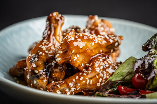 fried chicken wings in honey sour sauce with sesame seeds lie on a blue plate. background image