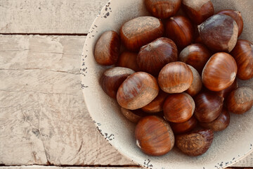 Close up chestnuts in a bowl on a wooden table with space for text.
