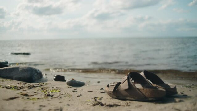 Women picks up sandals on stone beach along the ocean on a sunny day, Sandvik, Öland Sweden , close up wide