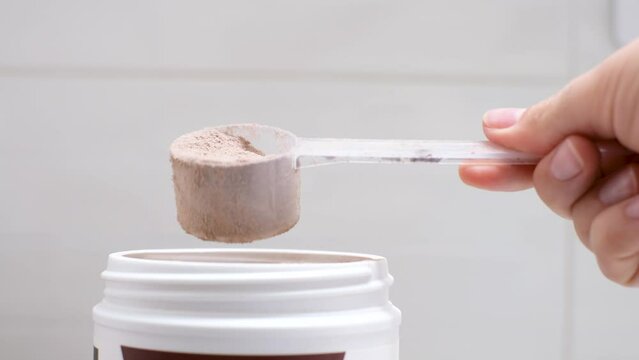 Female hand takes out protein in a scoop from jar on light background, side view.