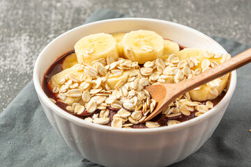 natural açaí with banana slices and oatmeal in a bowl over wooden table. top view