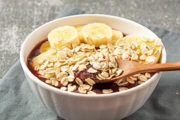 natural açaí with banana slices and oatmeal in a bowl over wooden table. top view