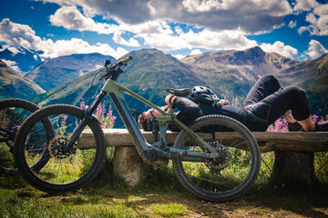 Electric bike in mountains. Bike rider resting on a bench. Bicycle trip in the mountains.