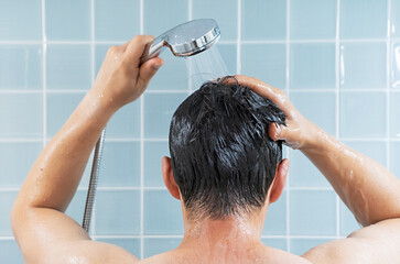 Man washing his hair in the shower against background of blue tiles, rear view.