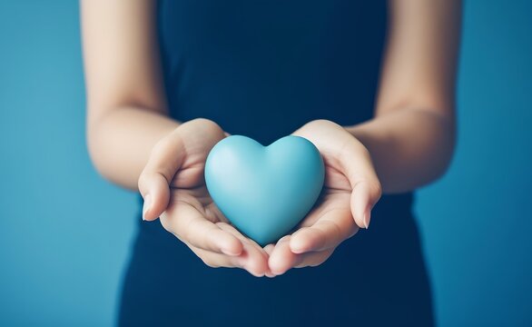 Young women hands holding blue heart on pastel background.